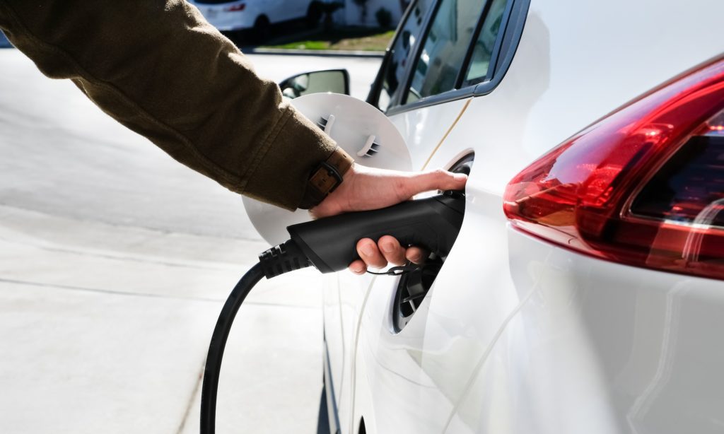 Hand is charging an electric car vehicle or EV at home charger.